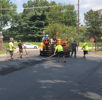 Paving machine with two operators is followed by two lute men and two shovel guys